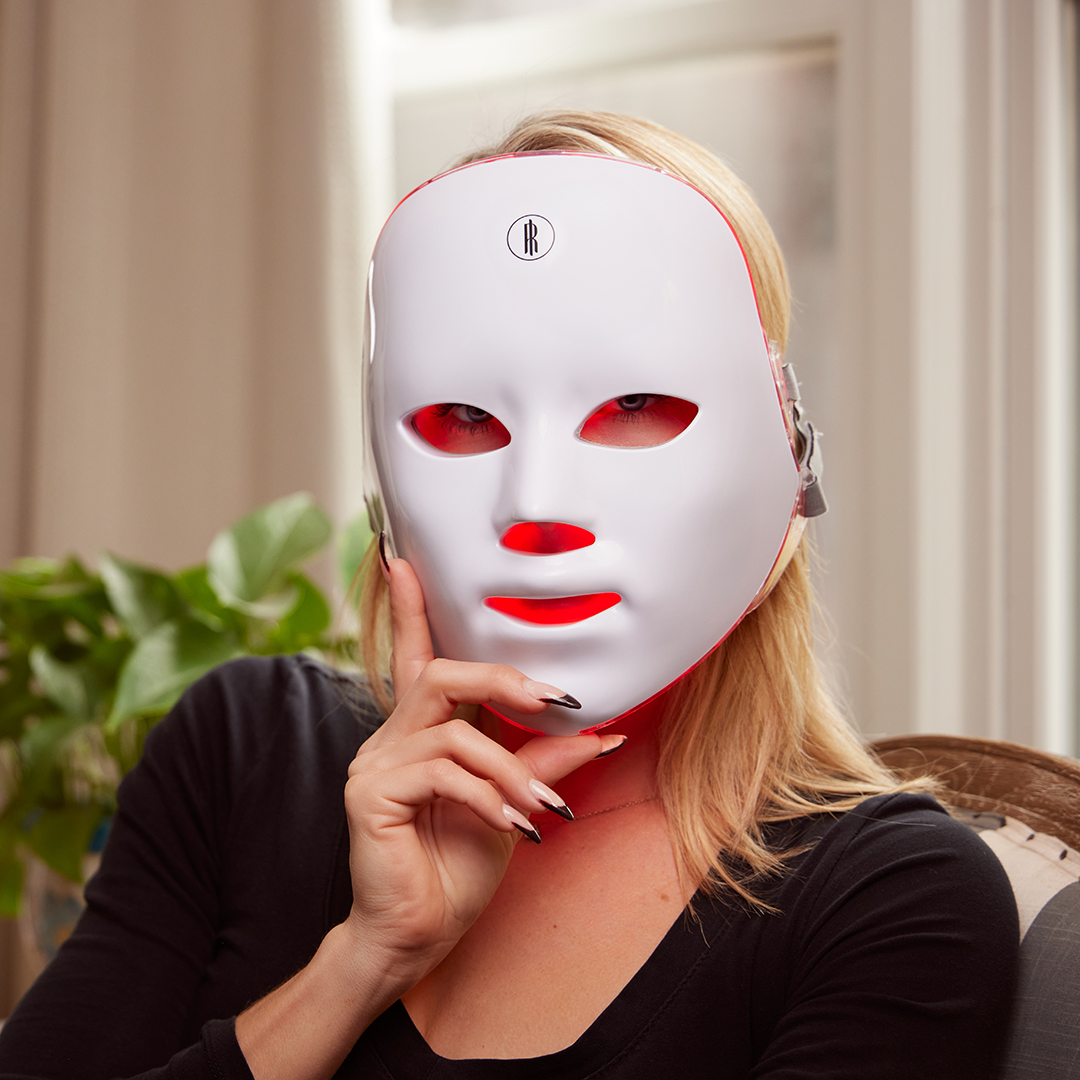 A woman with glowing skin using the wireless LED face mask in a relaxed setting.